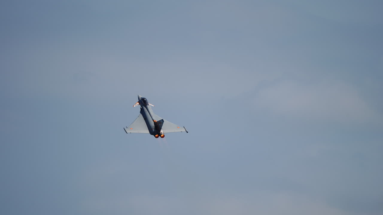 Modern jet fighter flying upward with visible engine exhaust smoke under cloudy sky