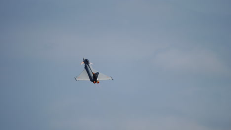 modern jet fighter flying upward with visible engine exhaust smoke under cloudy sky