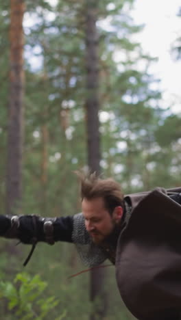 bearded man with flying cape falls down defeated by enemy in pine wood slow motion. killed knight at bloody battle. dramatic medieval fight scene