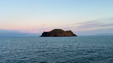 isla remota en vestmannaeyjar, islandia, bajo los suaves tonos del atardecer, el mar tranquilo en primer plano