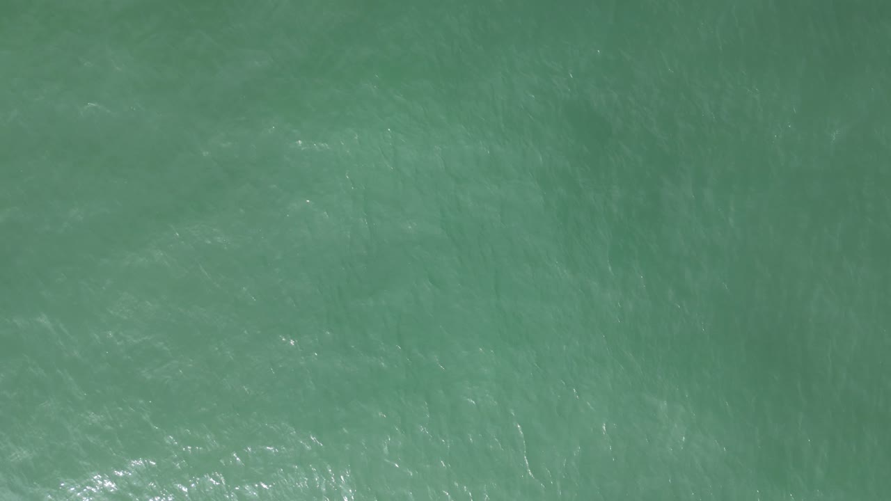 toma aérea de un mar turquesa con olas tranquilas que reflejan los rayos del sol