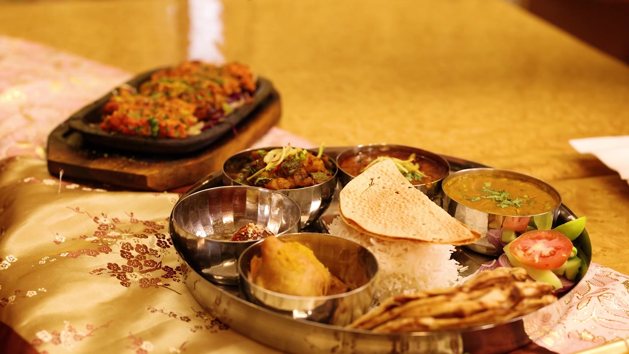 Nærbillede af hænder, der serverer forskellige indiske retter på et metal thali-fad.