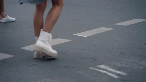 Woman-legs-crossing-street-on-crosswalk-with-crowd-in-city-background.