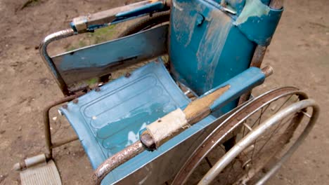 Vintage-retro-well-used,-worn-and-rusty-wheelchair-in-pale-blue-sitting-outside-in-the-garden,-forest,-jungle