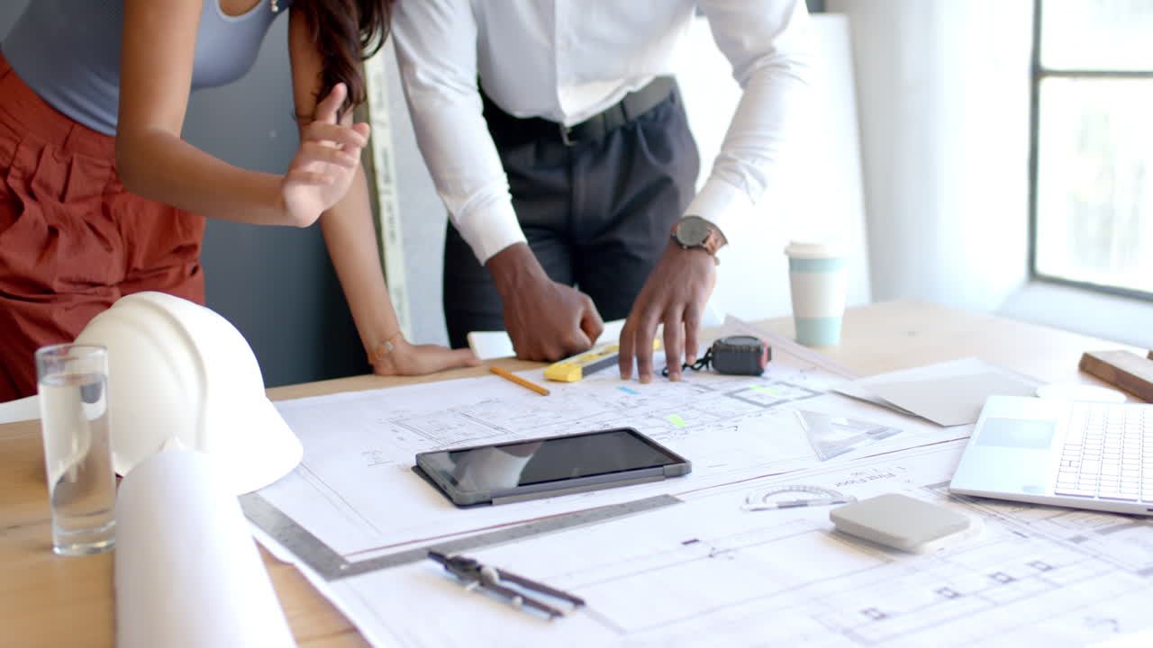 Discussing architectural plans, diverse colleagues using tablet and tools to review blueprints