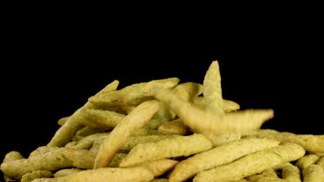 crispy puffed green pea chips fall onto a pile against a black background, captured in slow motion with even studio lighting and a static camera