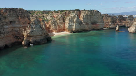 Cinematic-aerial-reveal-of-a-small-anchored-boat-near-rocky-cliffs-and-a-small-sand-beach