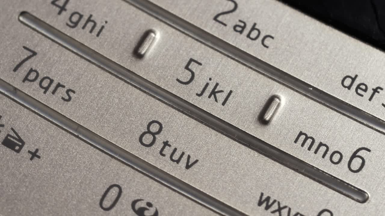 Rotating close up of silver mobile phone keypad with number and letter markings