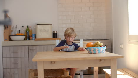 niño usando una tableta en la cocina, desde la puerta
