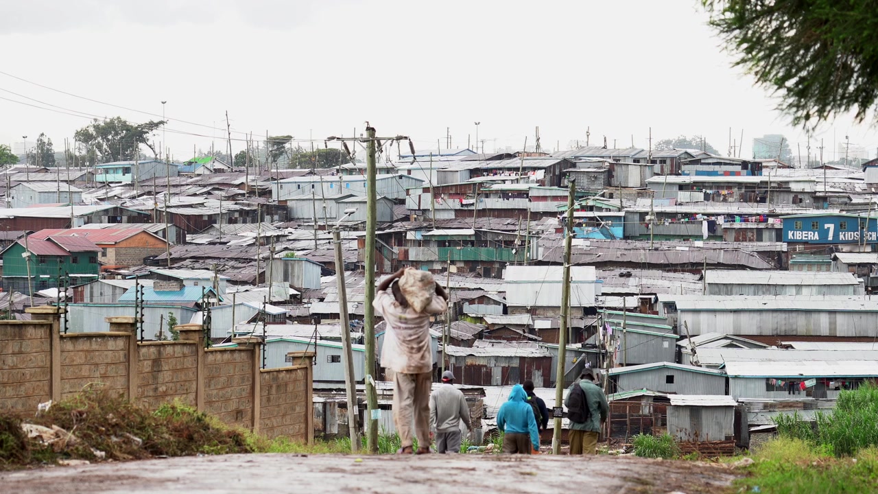 Menschen gehen auf einer Schotterstraße in Richtung eines Slums