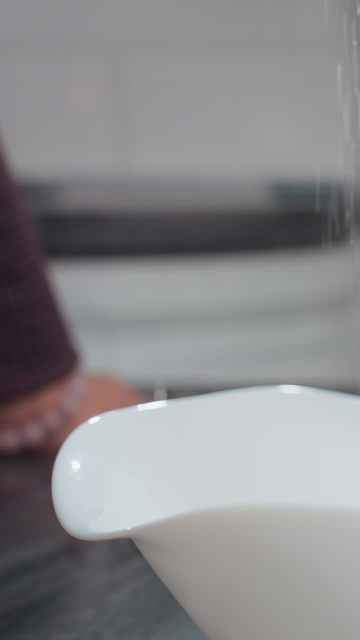 primer plano de una sustancia reluciente que se vierte en un cuenco blanco en un mostrador oscuro, una vista borrosa de una mano adornada con un brazalete de cuentas descansa en la mesa