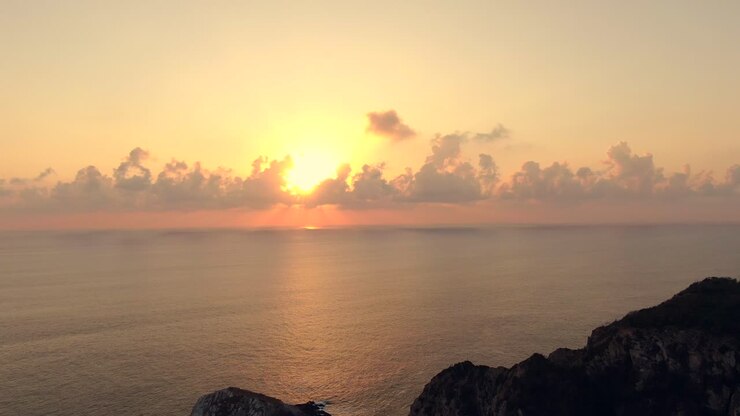 Bagliore arancione del tramonto dietro le nuvole sopra il mare tranquillo alla spiaggia di Maruata, Michoacán, Messico