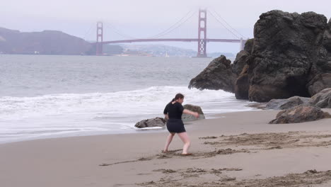 La-Mujer-Hace-Una-Danza-Interpretativa-Dramática-Y-Emocional-En-La-Playa,-El-Puente-Golden-Gate-En-El-Fondo