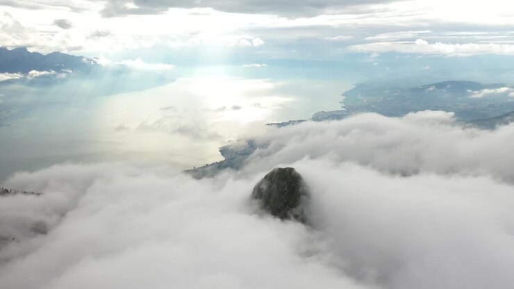 Aerial shot flying over the top of a mountain that is hidden by a bed of clouds near Rochere De Naye in Switzerland