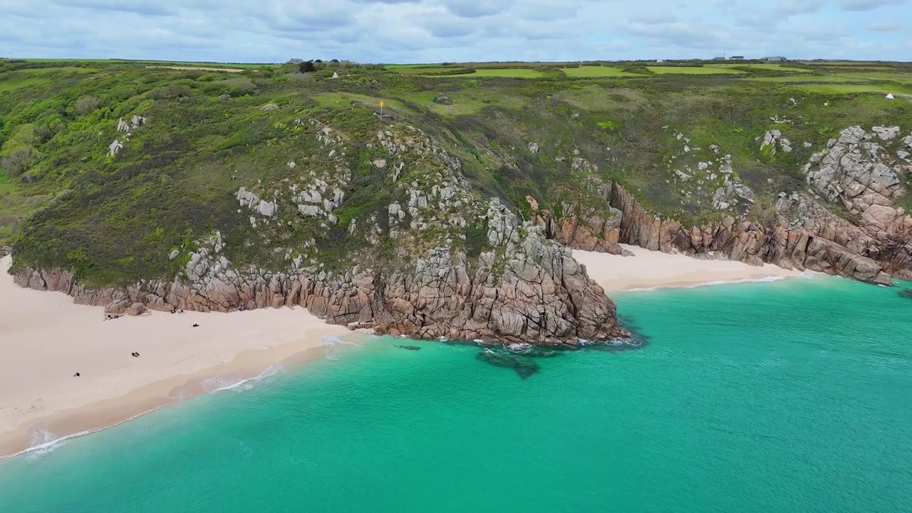 Kristal berraklığında deniz, sarp kayalıklar ve büyüleyici kıyı manzarasına sahip İngiltere, Cornwall'daki Porthcurno Plajı'nın sinematik havadan videosu.