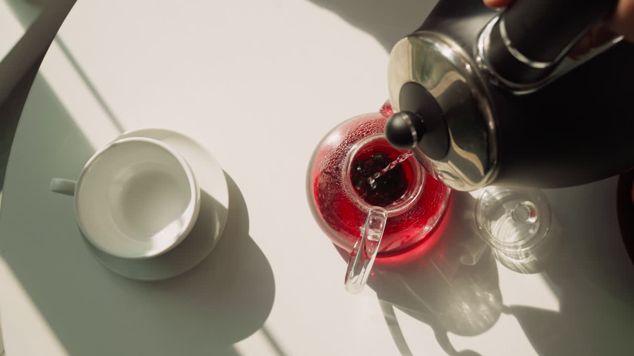 테이블 위에 뜨거운 물로 차 비를 채우기: 부에서 전기 비에서 흐르는 히비스쿠스 차를 양조하는 과정