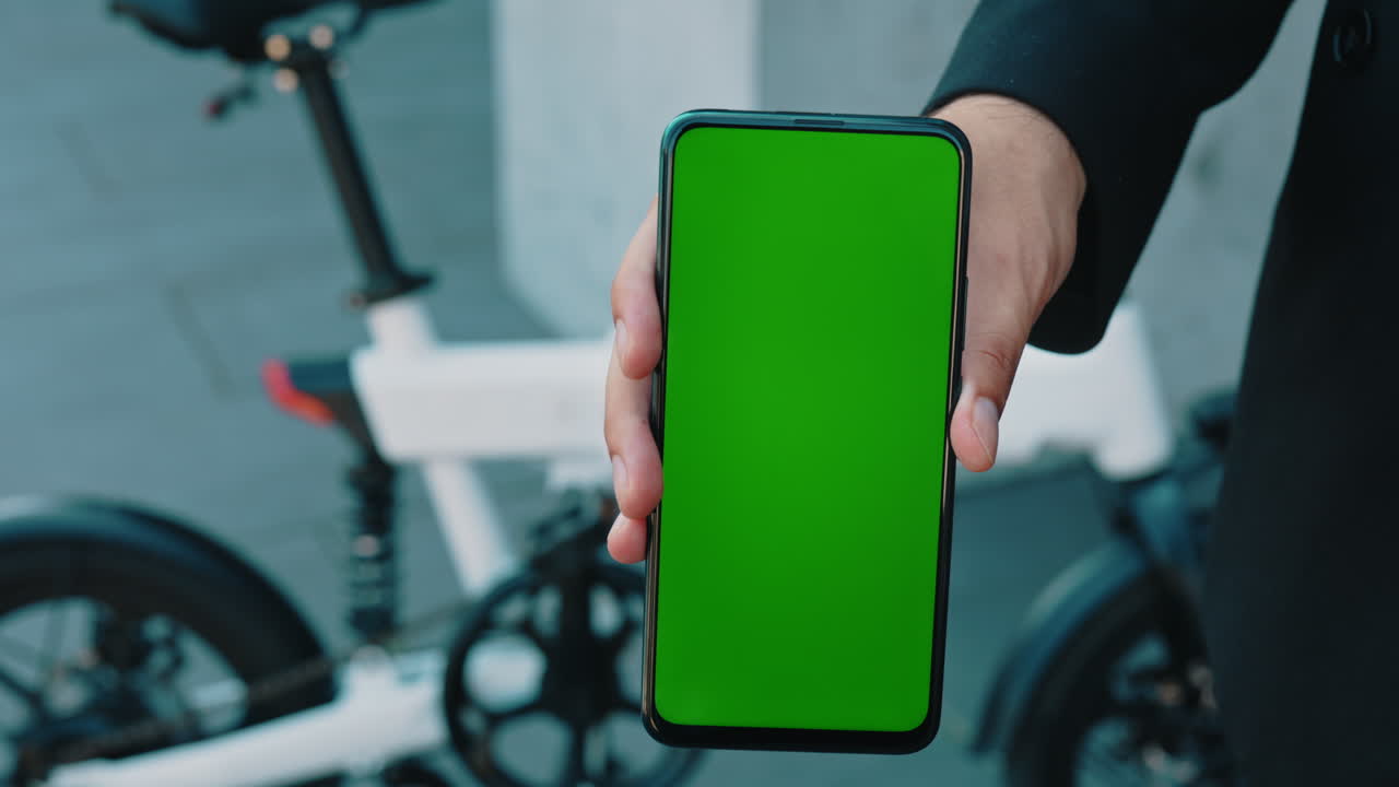 Person holding smartphone with green screen next to a bicycle