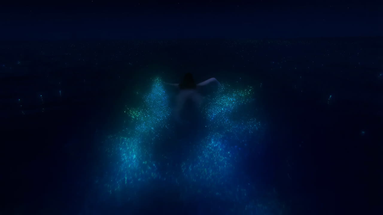 A person swimming amidst glowing bioluminescent particles in dark water