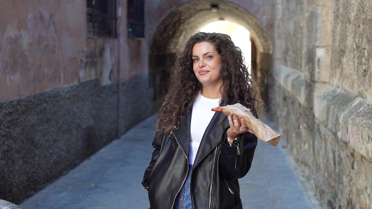 Una giovane donna con i capelli ricci, vestita con un'elegante giacca di pelle, posa in un contesto urbano.
