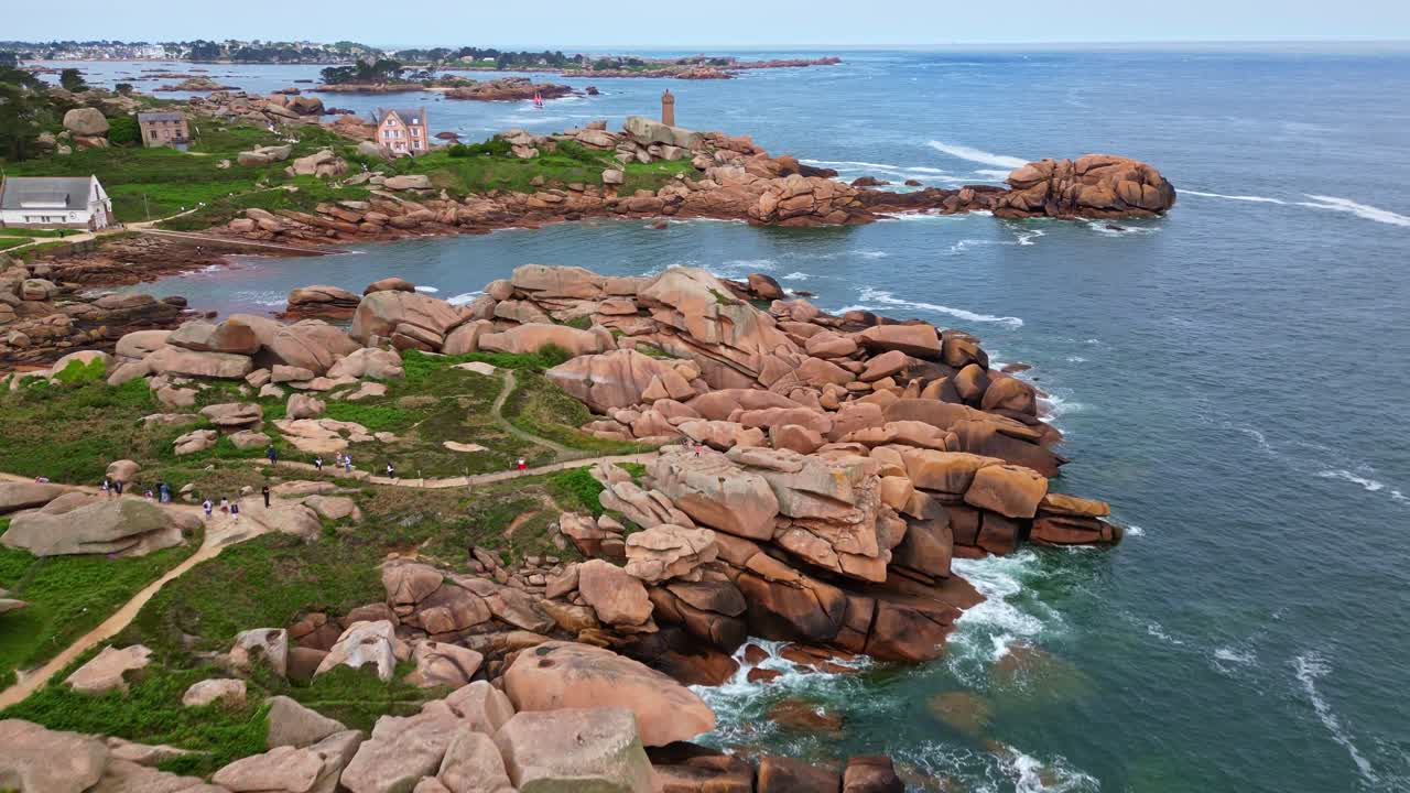 Pink Granite Coast in Ploumanac'h, rugged boulders, iconic Mean Ruz lighthouse, Brittany coastline, France. Aerial drone forward