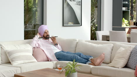 relaxing on sofa, man in turban talking on smartphone in living room
