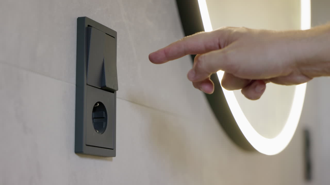 Man switching bathroom mirror light on and off using wall switch, modern bathroom lighting control
