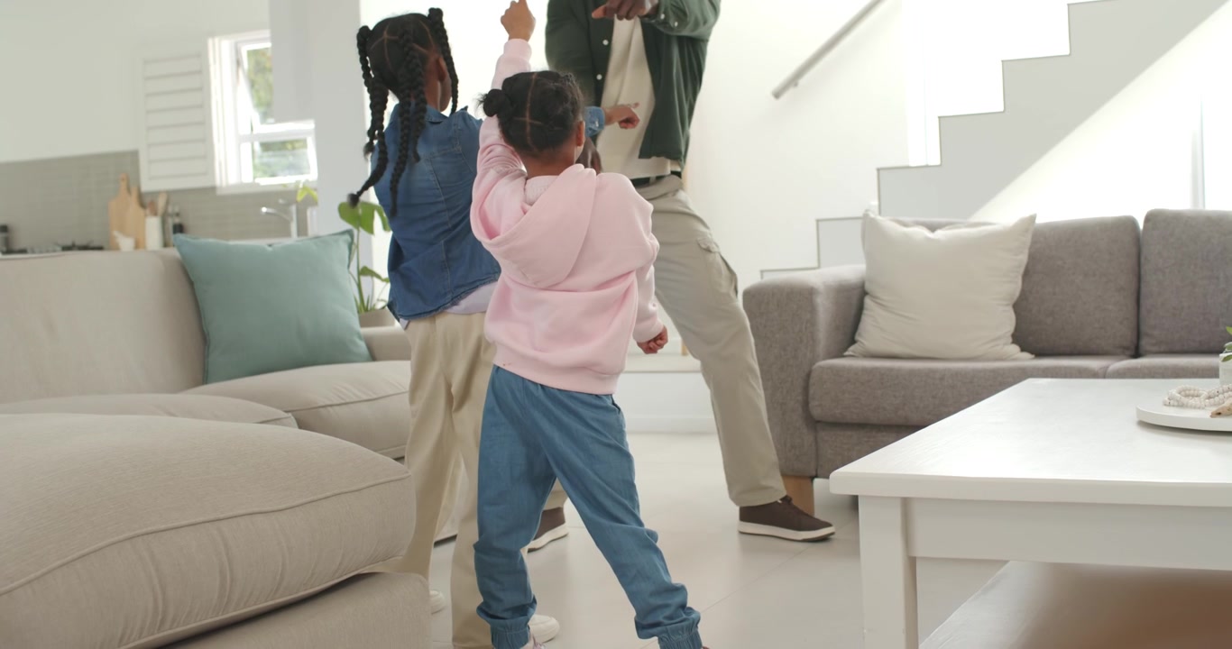 African American family dad leading two youth girls, raising arms guiding dance at home near sofa