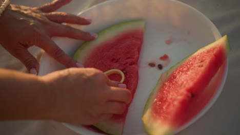 primer plano de la mano presionando un cortador en forma de amor en una jugosa rebanada de sandía en un plato blanco, contrastando la corteza verde y la carne roja vibrante, capturando un momento creativo y lúdico de verano