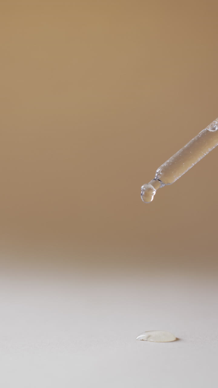 Vertical video of make up pipette and drops of serum with copy space on brown background