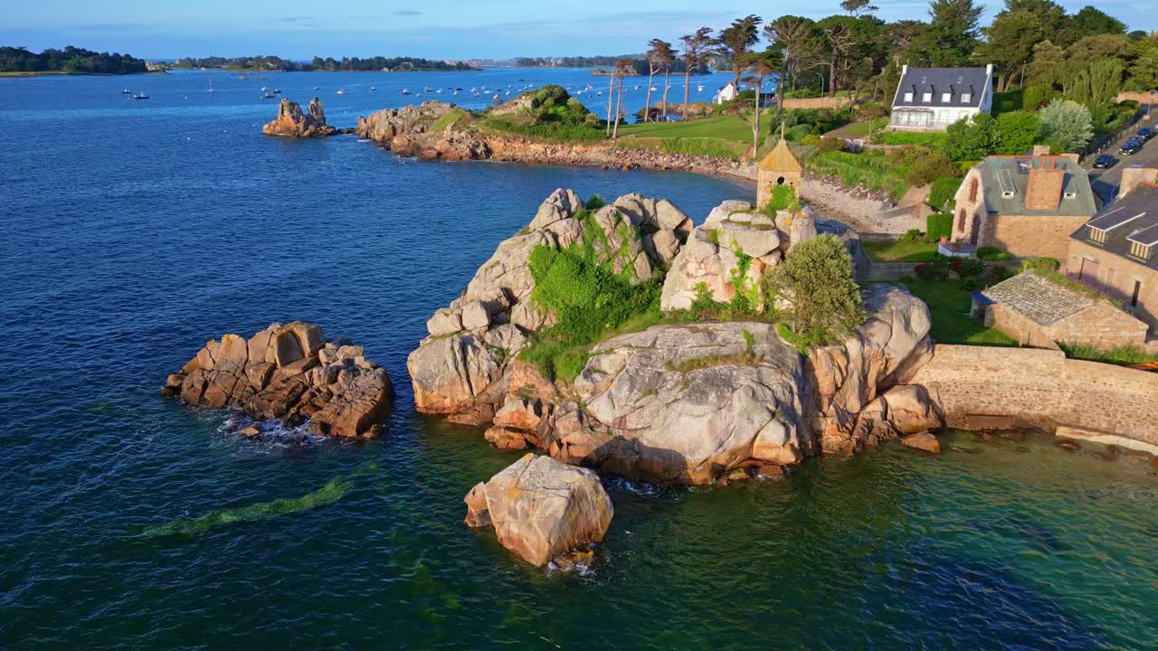 Rocky outcrop the iconic Sentinel Oratory and houses nestled along the beautiful seashore in vivid blue coastal waters at Port Blanc, Côtes-d'Armor, Brittany, France.