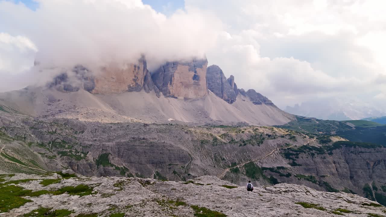 Aerial wide shot, drone orbiting left around solo traveler in the Dolomite Alps