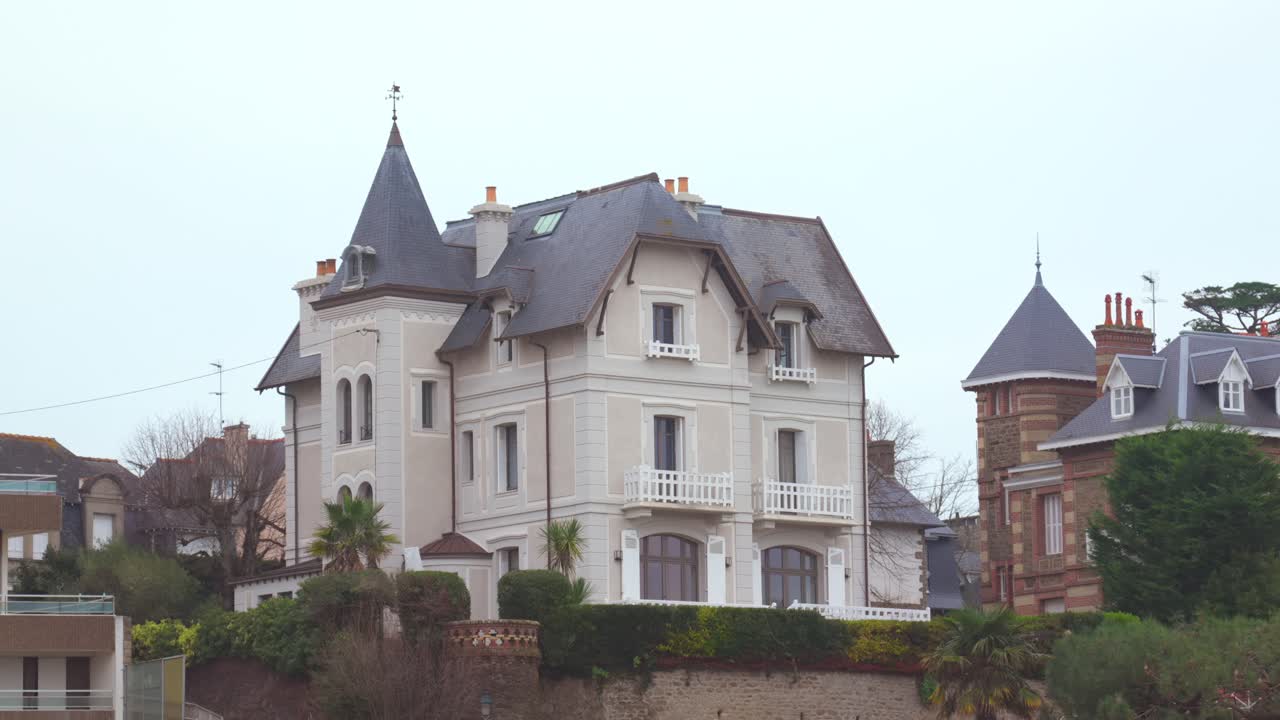 A large traditional Dinard villa is seen from the beach under a grey winter sky. The elegant architecture stands out against the moody, overcast coastal atmosphere.