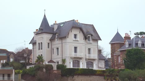 a large traditional dinard villa is seen from the beach under a grey winter sky. the elegant architecture stands out against the moody, overcast coastal atmosphere.