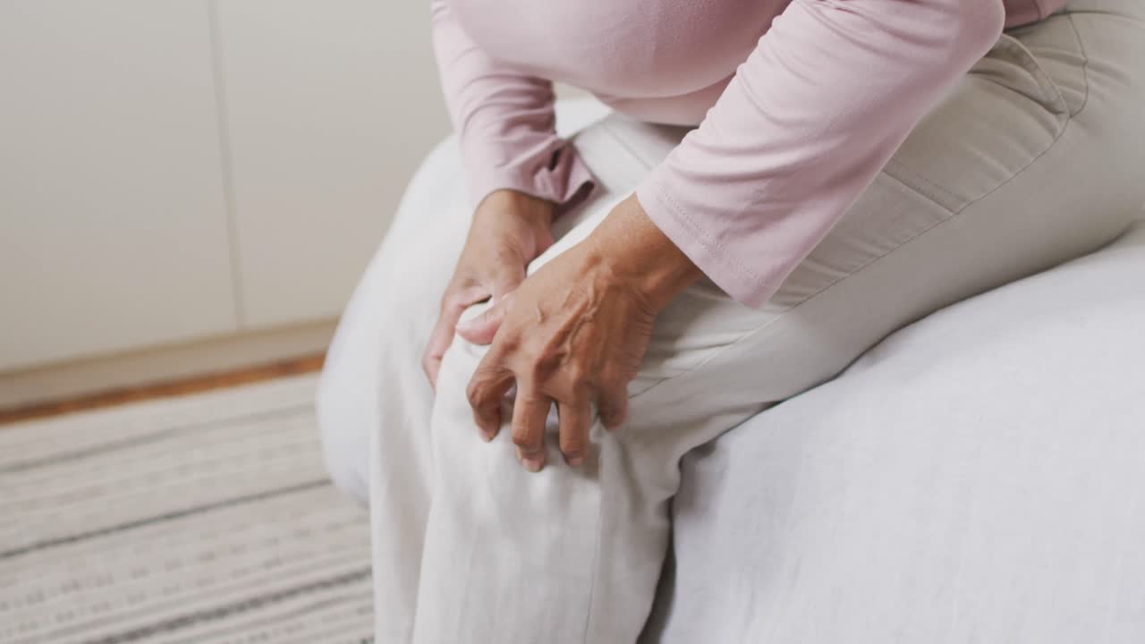 sección media de una mujer mayor afroamericana sosteniendo su pierna en el dolor en casa