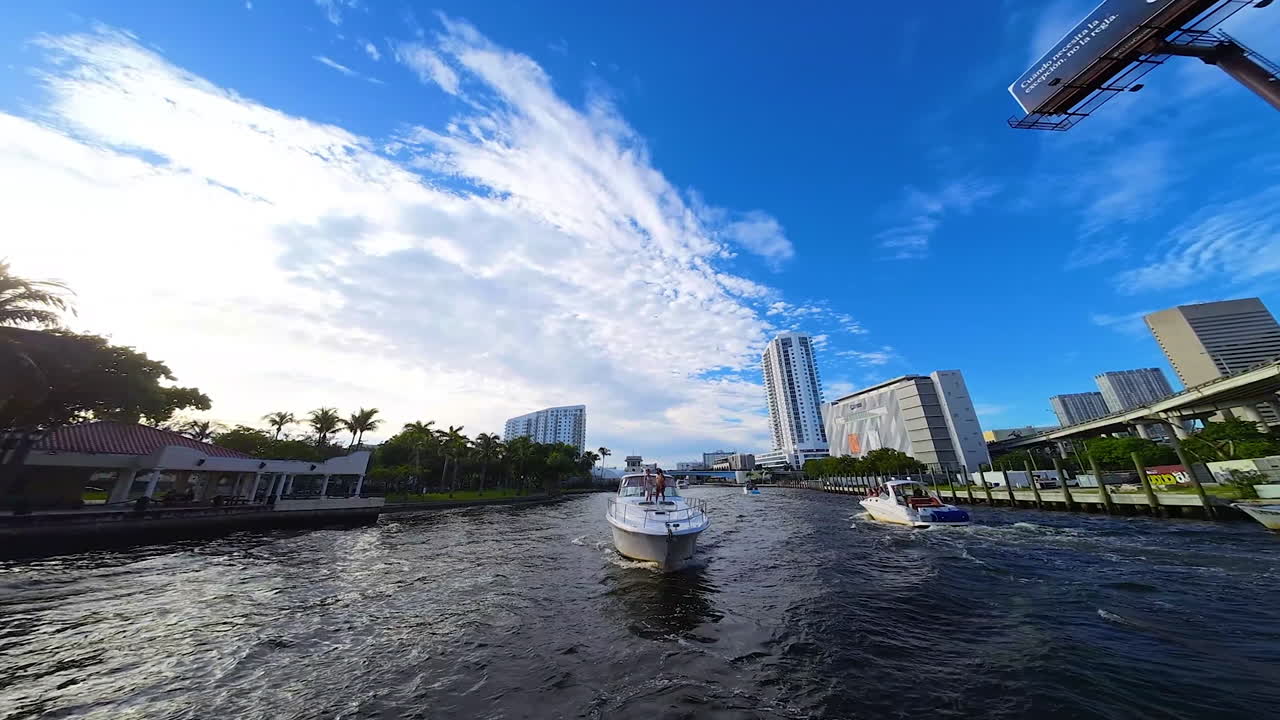 Front view of a yacht moving towards camera by the narrow river. FPV drone footage in American city with low angle view at the beautiful sky with white clouds.