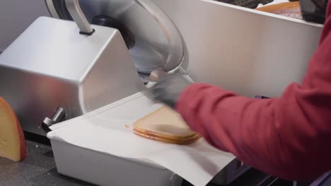 un trabajador de delicatessen uniformado y enguantado corta queso con un cortador industrial