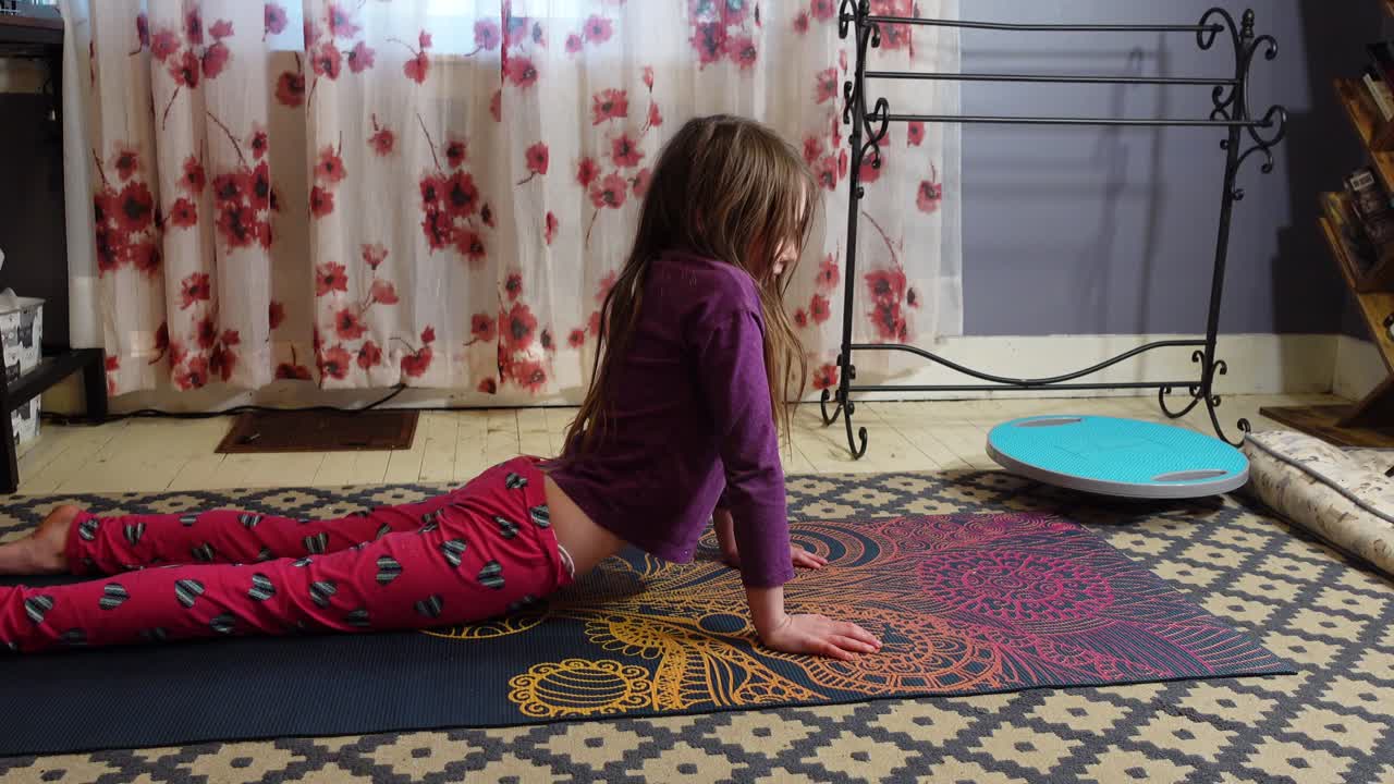 niña en un partido de yoga con el pelo largo practicando yoga y haciendo estiramientos dentro junto a una ventana cálida con cortinas brillantes 4k tiro medio horizontal inmóvil