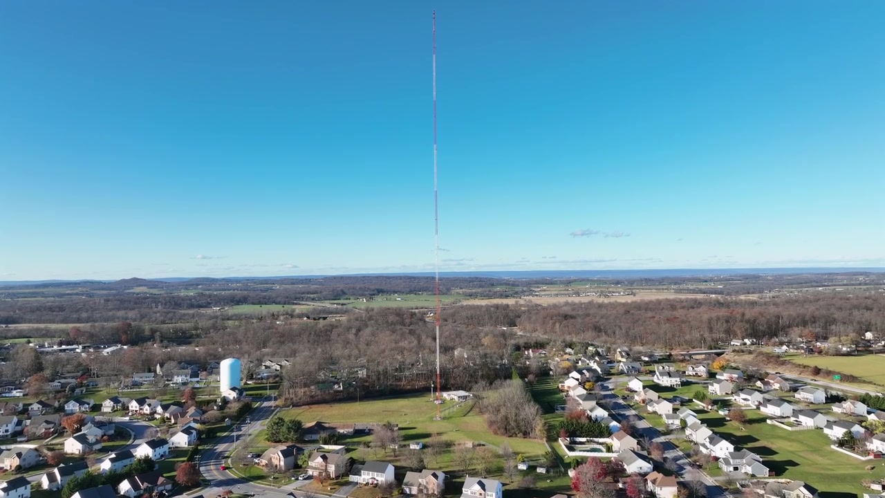 Luftflyvning over et forstadsboligområde på en solrig dag med blå himmel. Huse og hjem i forstæderne. Sendemast med silo og bondegård. Motorvejstrafik på amerikansk interstate. Vidvinkelbillede