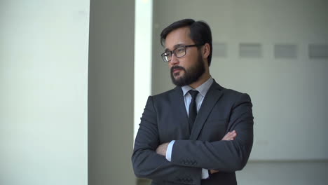 close up of bearded businessman standing at the window with his arms crossed and looking straight at camera