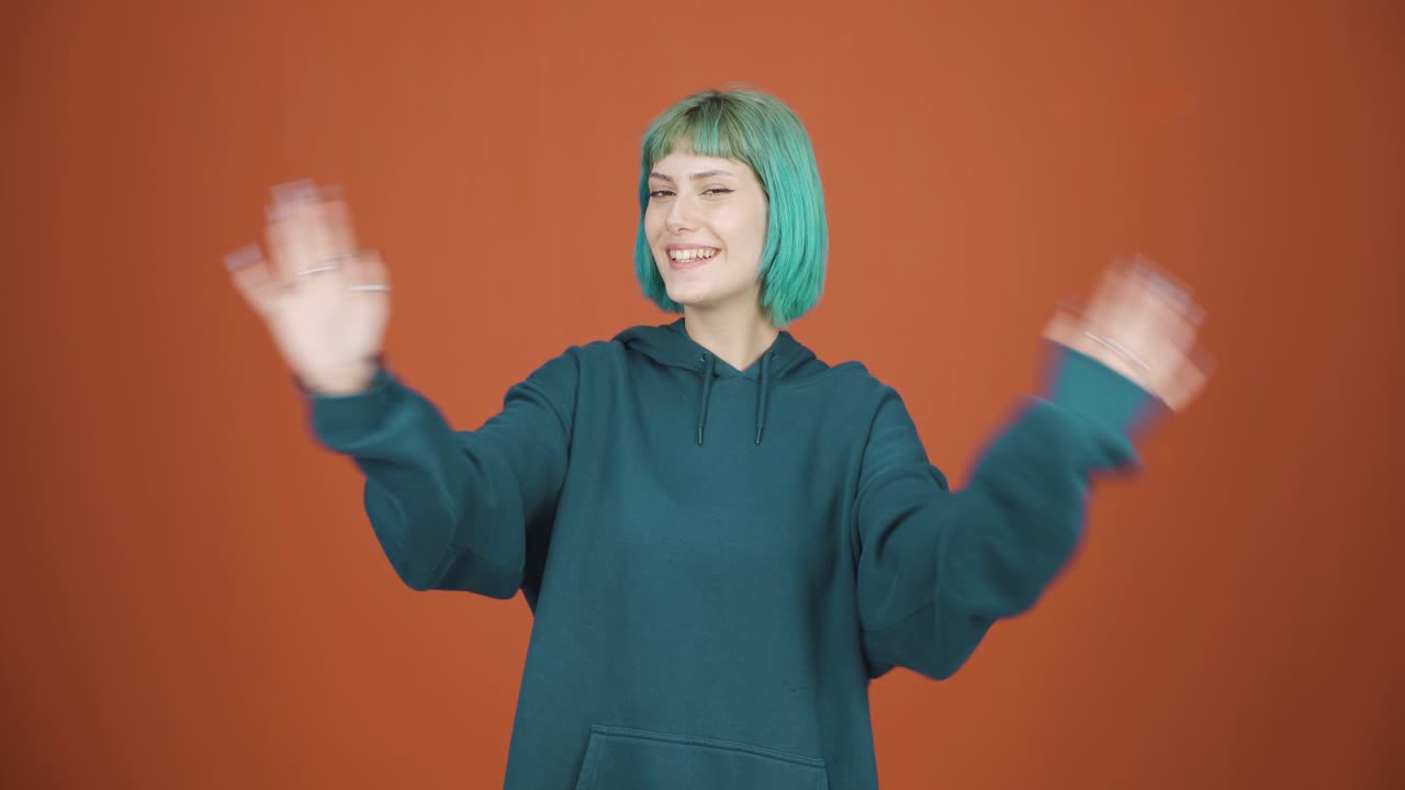 행복한 젊은 여성이 카메라를 향해 손을 흔들고 있습니다.