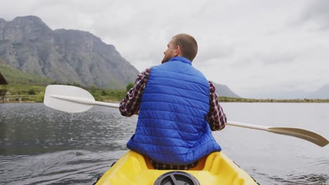 Caucasian-man-having-a-good-time-on-a-trip-to-the-mountains,-kayaking-on-a-lake,-holding-a-paddle