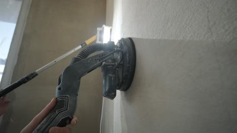 action shot of construction work, showing a hand guiding a power sander on a wall, part of the process of smoothing surfaces for a fine finish in renovation