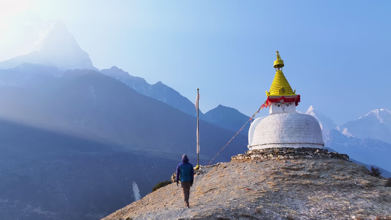 A male tourist runs toward Buddhist stupa in Dingboche, Khumbu region, Nepal. Ama Dablam peak rises in backdrop as drone captures scenic mountain ranges and relaxing Himalayan landscape, clear weather