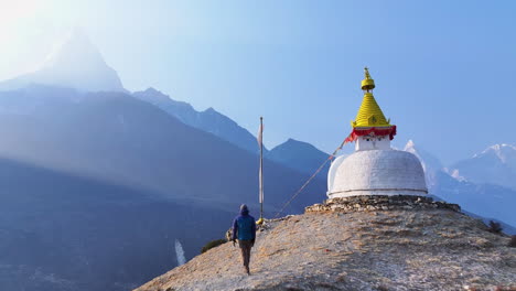 a male tourist runs toward buddhist stupa in dingboche, khumbu region, nepal. ama dablam peak rises in backdrop as drone captures scenic mountain ranges and relaxing himalayan landscape, clear weather