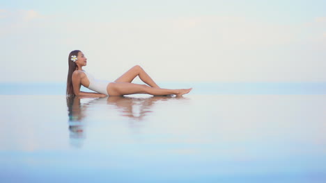 Sexy-exotic-woman-in-swimsuit-at-infinity-swimming-pool,-flower-in-hair,-endless-horizon,-full-frame-slow-motion