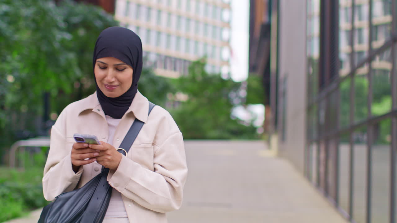 Muslim Businesswoman Wearing Hijab Going To Work Standing Outside Modern Office Looking At Mobile Phone 3
