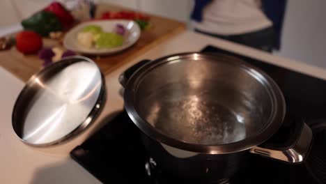 saucepan with boiling water against crop woman and fresh vegetables