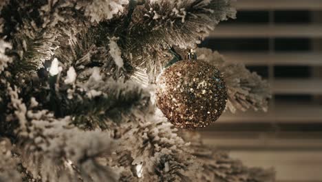 close up of a gold christmas ornament on a snow frosted christmas tree