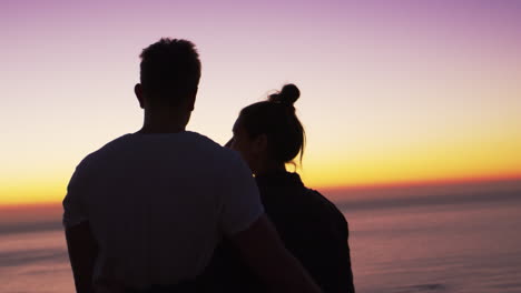 Couple-standing-on-a-beach-by-the-sea-at-sunset