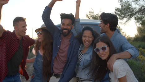 Friends-on-a-road-trip-cheering-to-camera-outside-their-van